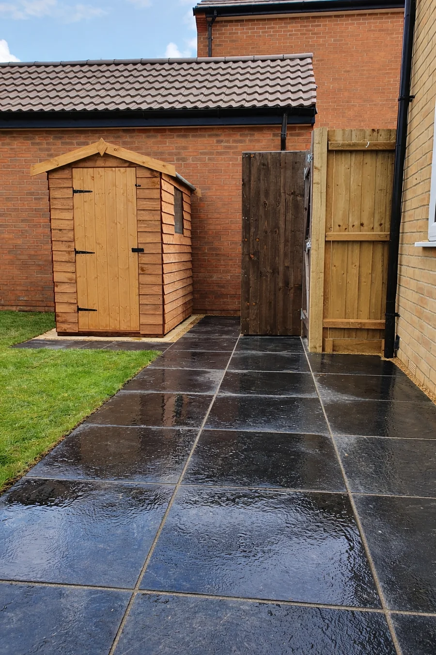 Completed black paving area beside a garden shed and gate